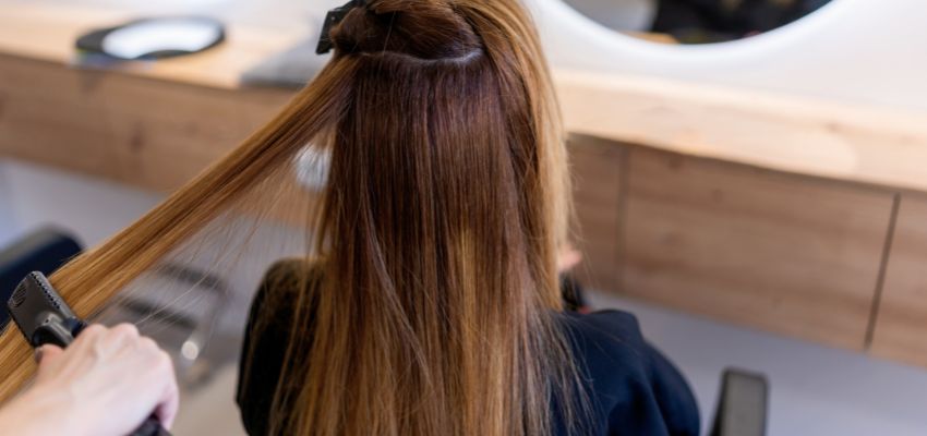 Hair stylist performing a keratin treatment on a client in a salon.