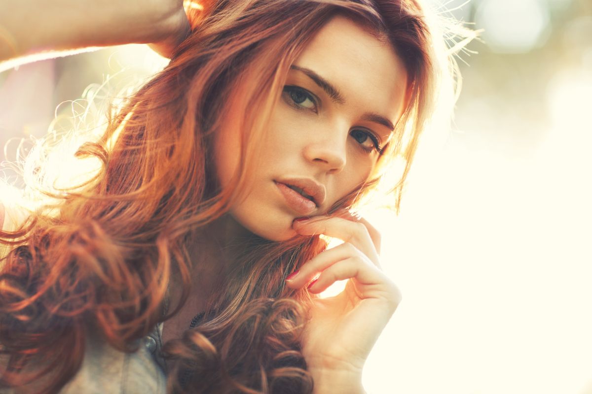 Woman with shiny auburn hair color posing under natural light to highlight warm red-brown tones.