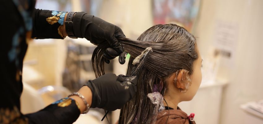 Hairstylist applying auburn hair color to a client’s hair at a salon for a rich, vibrant finish.