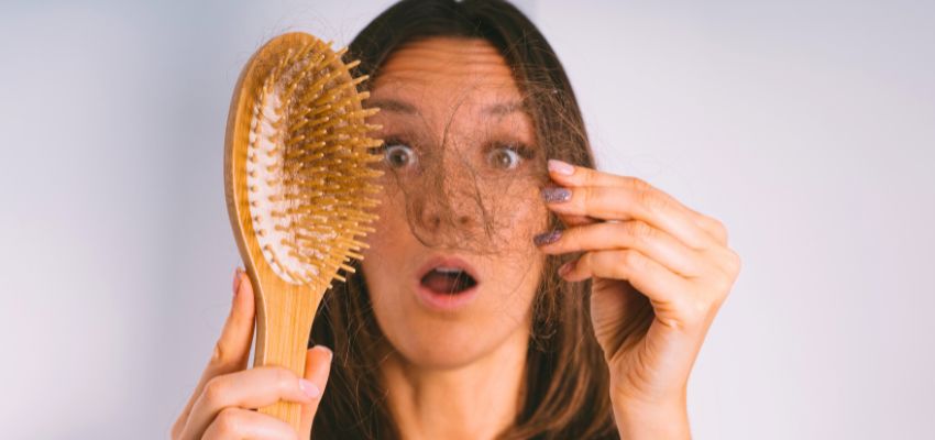 Does brushing hair stimulate growth: woman shocked by excessive hair shedding on her wooden brush, highlighting common concerns about brushing and hair loss