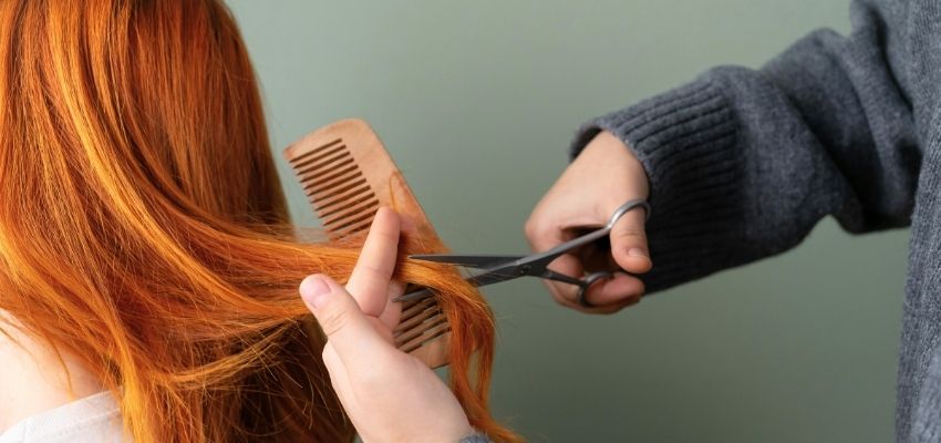 How often should you trim your hair: detailed shot of trimming bright red hair with wooden comb and sharp scissors to remove split ends and maintain length
