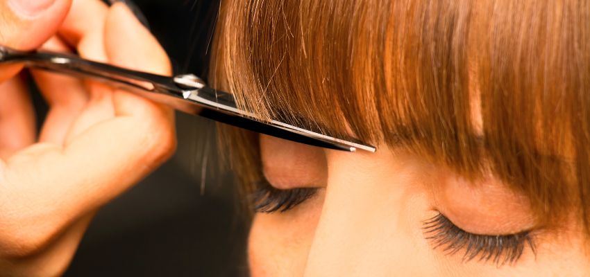 The hairstylist is trimming the client's bangs.