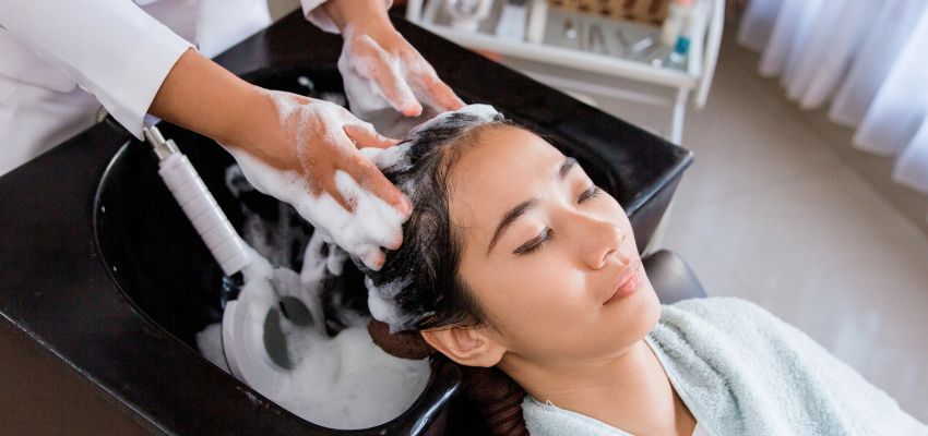 is-sodium-lauryl-sulfate-bad-for-hair2 Woman relaxing during a professional hair wash with foamy shampoo in a salon sink, hands massaging scalp, representing cleansing process when asking "is sodium lauryl sulfate bad for hair