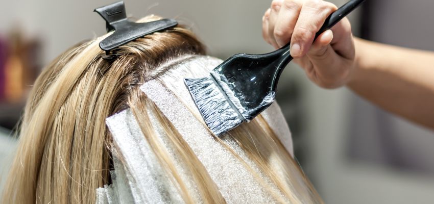 A hairstylist applies precise bleach with a brush during the babylights vs highlights process on blonde hair sections.