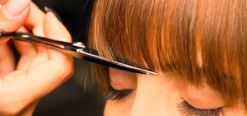 Close-up of scissors trimming bangs while demonstrating what is a fringe haircut