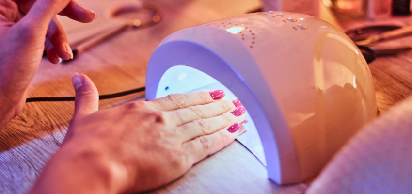 how-to-dry-gel-nail-polish-without-uv-light1 Hands curing red gel nail polish under a UV lamp, contrasting common methods with how to dry gel nail polish without UV light.