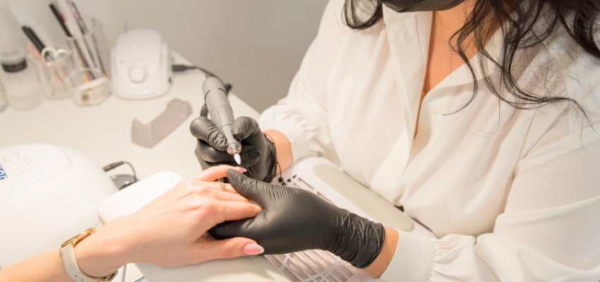 Nail technician using an electric file during a professional manicure, demonstrating what does builder gel do in nail strengthening treatments.